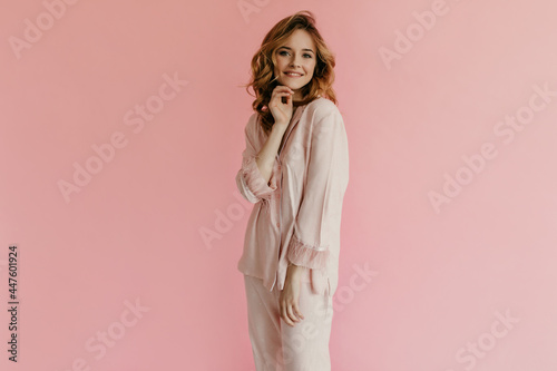 Attractive woman with curly hairstyle in pink stylish pajamas posing on isolated background. Girl in modern clothes looking into camera..