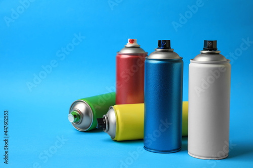 Cans of different graffiti spray paints on light blue background, space for text