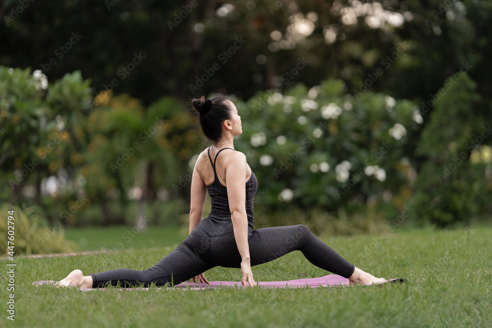 A confident middle-aged Asian woman in a sports outfit doing yoga exercise on the yoga mat outdoor in the backyard in the morning. Young woman doing yoga exercise outdoor in nature public park