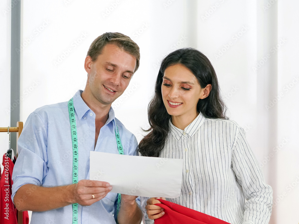 Fashion designer room, man and woman working in home base cloth design business. A male tailor show a shirt design pattern in a paper to young customer while choosing the fabric. Fashion designer room, man and woman working in home base cloth design business. A male tailor show a shirt design pattern in a paper to young customer while choosing the fabric.