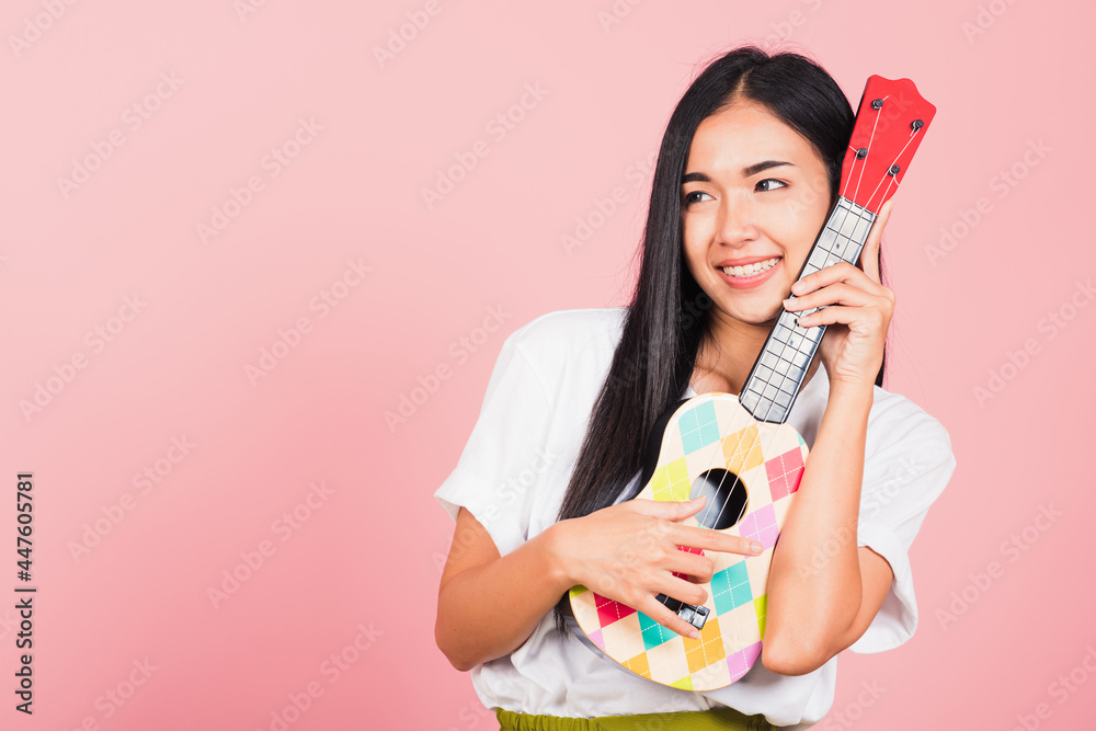 Portrait of happy Asian beautiful young woman teen confident smiling face hold acoustic Ukulele guitar, female playing Hawaiian small guitar, studio shot isolated on pink background, with copy space Portrait of happy Asian beautiful young woman teen confident smiling face hold acoustic Ukulele guitar, female playing Hawaiian small guitar, studio shot isolated on pink background, with copy space