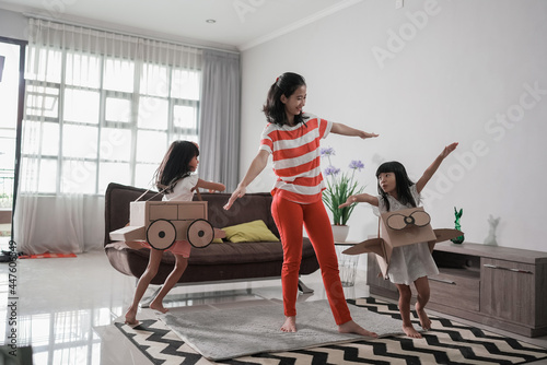 girl playing with cardboard toy airplane at home with mother