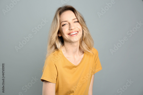 Portrait of happy young woman with beautiful blonde hair and charming smile on grey background © New Africa