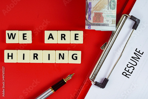 Business concept - layout of fake money, pen, resume on clipboard and tiles with text We are hiring