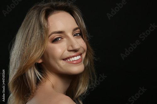 Portrait of happy young woman with beautiful blonde hair and charming smile on black background. Space for text