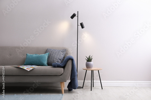 Stylish room living interior with comfortable sofa and lamp near white wall