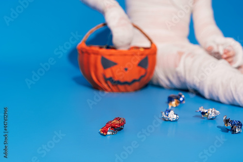 Photography Child in mummy costume eats candies from basket in the form of pumpkin against b