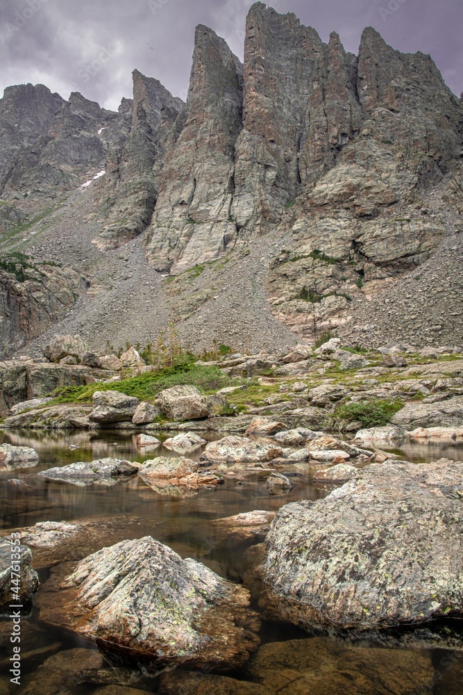 Obraz premium View of sky pond in Rocky Mountain National Park in Colorado. Sharp teeth-like peaks can be seen as well as the pond water with rocks and a purple sky.
