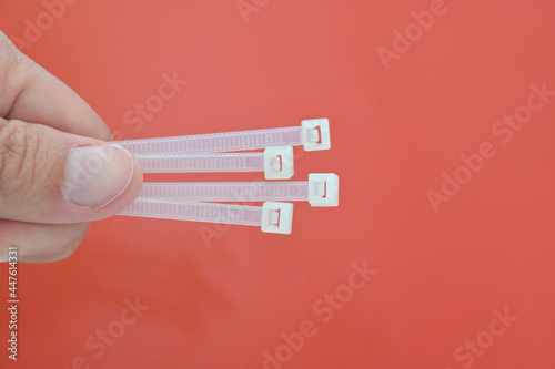 A person is holding white cable ties against a red background.