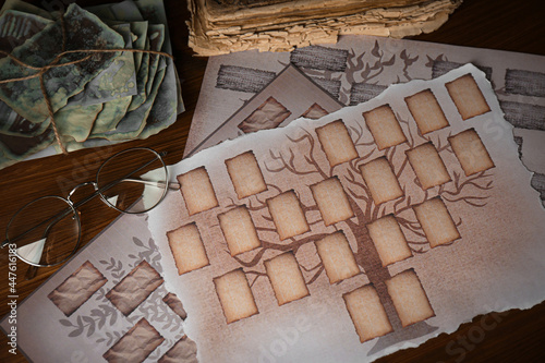 Papers with family tree templates, photos and glasses on wooden table, flat lay