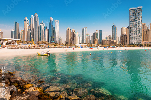 Luxurious and spectacular sandy beach with vacationers in the Dubai Marina and JBR area with tall skyscrapers and hotels in the background