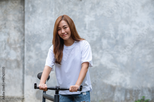 Portrait image of a beautiful young asian woman wearing white t-shirt and jean short pant with bicycle and concrete wall background