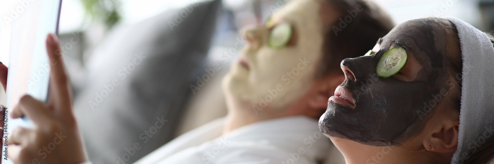 Young man and woman lying on couch with moisturizing face masks Young man and woman lying on couch with moisturizing face masks