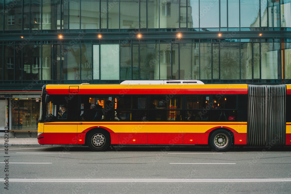 A yellow and red articulated bus parked near business center in the city. Bendy. Tandem. Vestibule bus. Stretch bus. An accordion bus. Articulated vehicle used in public transportation