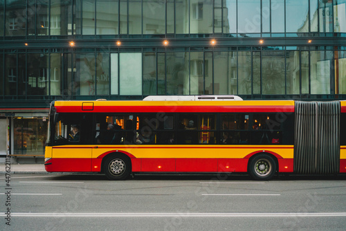 A yellow and red articulated bus parked near business center in the city. Bendy. Tandem. Vestibule bus. Stretch bus. An accordion bus. Articulated vehicle used in public transportation