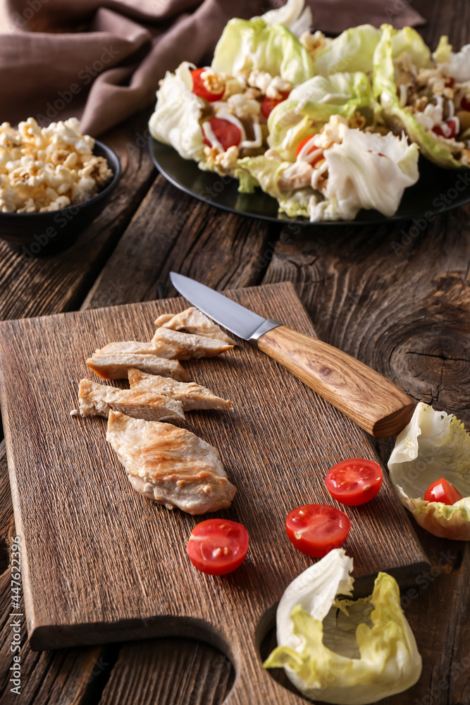 Board with sliced chicken meat on wooden background