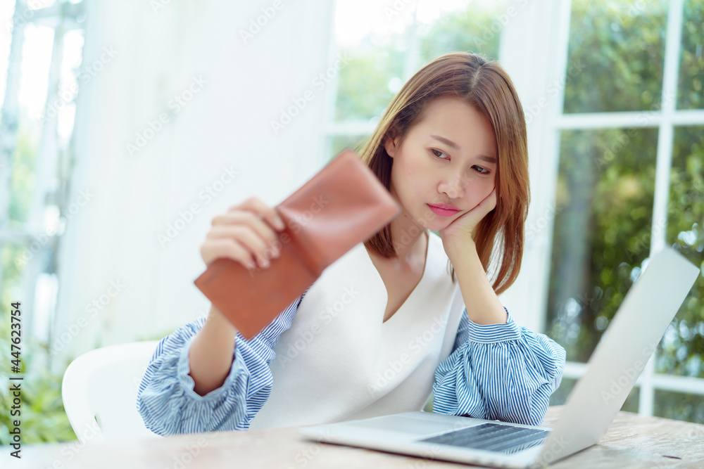 Half-body portrait of an Asian woman in a white shirt sitting in a bakery examining her purse for money with a stressed, unhappy face. Half-body portrait of an Asian woman in a white shirt sitting in a bakery examining her purse for money with a stressed, unhappy face.