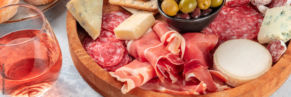 Rose wine with charcuterie and cheese board panorama. Italian antipasti panoramic banner with a wineglass and prosciutto di Parma ham, salami, gorgonzola and olives