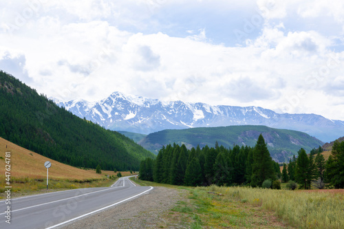 snowy peaks of mountains against the background of clouds and the road stretching into the distance