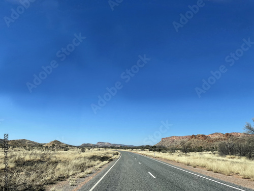 The stunning MacDonnell Ranges, outside Alice Springs, Northern Territory, Australia. With long roads and open plains with distant mountains.