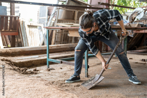 Male carpenter worker using shovel with sawdust in carpentry workshop. Carpenter working his job at his workplace