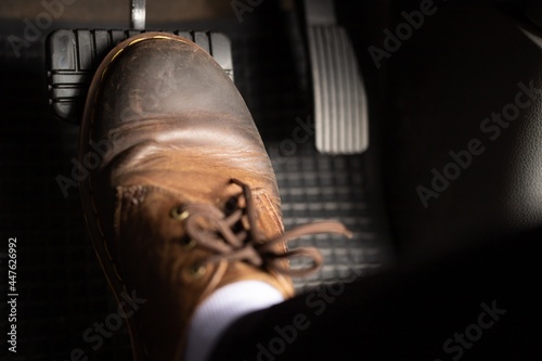 A man in brown leather shoes is stepping on the brakes of a car.