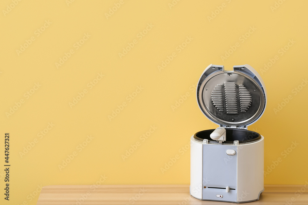 Modern deep fryer on table near color wall Modern deep fryer on table near color wall