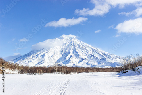 Russia, Kamchatka Volcanoes Natural Park. A snow-covered road along a frozen riverbed in the direction of an icy volcano. Winter hiking to the Avachinsky pass.