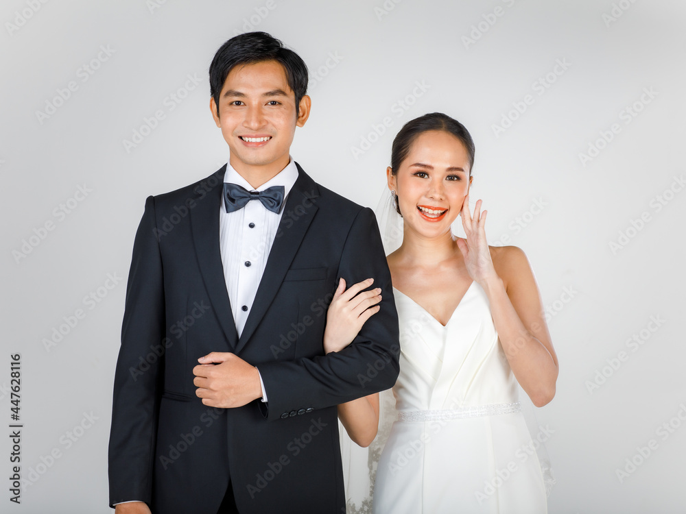 Young attractive Asian couple, bride and groom, woman wearing white wedding dress. Man wearing black tuxedo, standing arm in arm together. Concept for pre wedding photography Young attractive Asian couple, bride and groom, woman wearing white wedding dress. Man wearing black tuxedo, standing arm in arm together. Concept for pre wedding photography