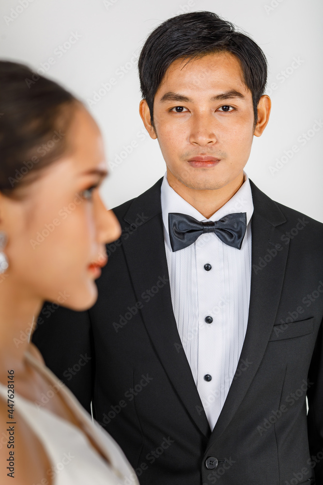 Selective focus of young attractive Asian man wearing black tuxedo and blurry woman in foreground wearing wedding gown. Concept for bride and groom pre wedding photography Selective focus of young attractive Asian man wearing black tuxedo and blurry woman in foreground wearing wedding gown. Concept for bride and groom pre wedding photography