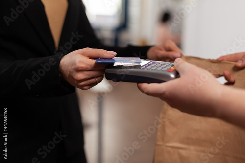 Close up of business woman holding credit card of pos, using contactless technology. Customer paying for their order with a credit card. Holding takeaway food in paper bag.