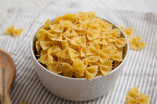 Dry Organic Farfalle Pasta in a Bowl on a white wooden background, side view.