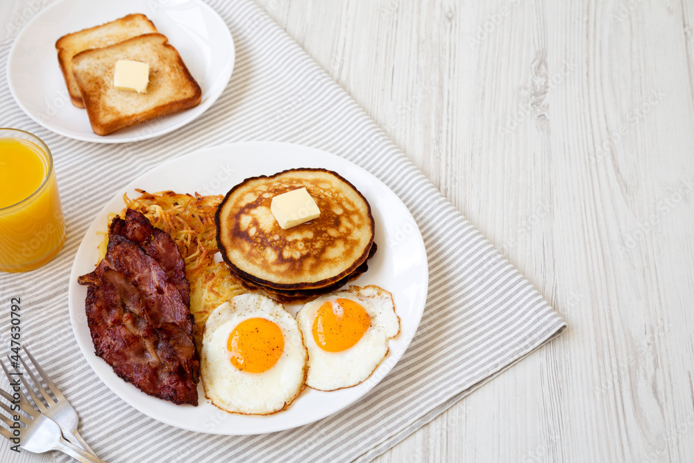Full American Breakfast with Bacon, Hash Browns, Eggs and Pancakes on a plate on a white wooden background, side view. Space for text. Full American Breakfast with Bacon, Hash Browns, Eggs and Pancakes on a plate on a white wooden background, side view. Space for text.
