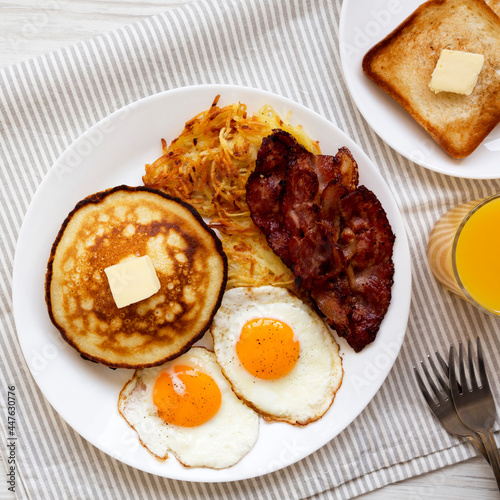 Full American Breakfast with Bacon, Hash Browns, Eggs and Pancakes on a plate on a white wooden table, top view. Flat lay, overhead, from above.