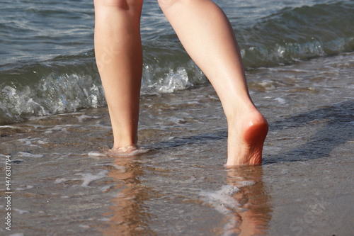 Barefoot girl running by the sand in the sea waves. Naked female legs in water, beach vacation