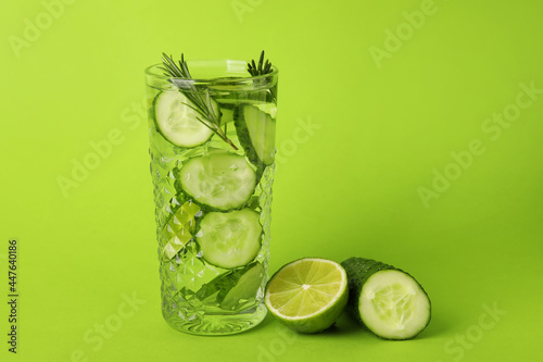 Glass with cucumber lemonade on color background