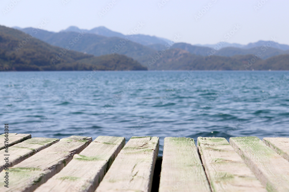 Beach vacation on the sea, background for summer holidays and travel. View from old wooden pier to deep blue water and misty mountains covered with forest