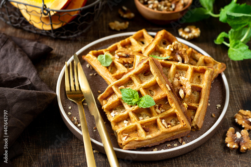 Homemade pumpkin waffles with walnuts in a plate on a brown culinary background closeup