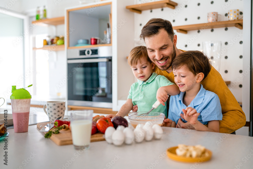 Happy single father with kids having fun and preparing healthy food in kitchen at home.