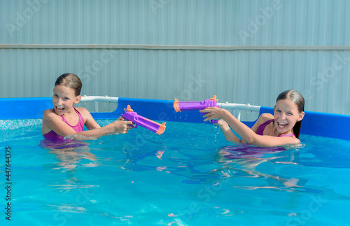 Two tween caucasian girls with water guns toy fight game in pool