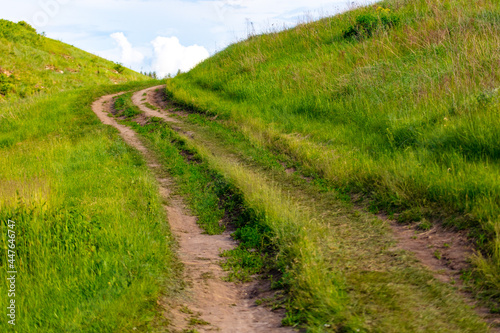 Dirt road in green grass on a mountainside. © schankz
