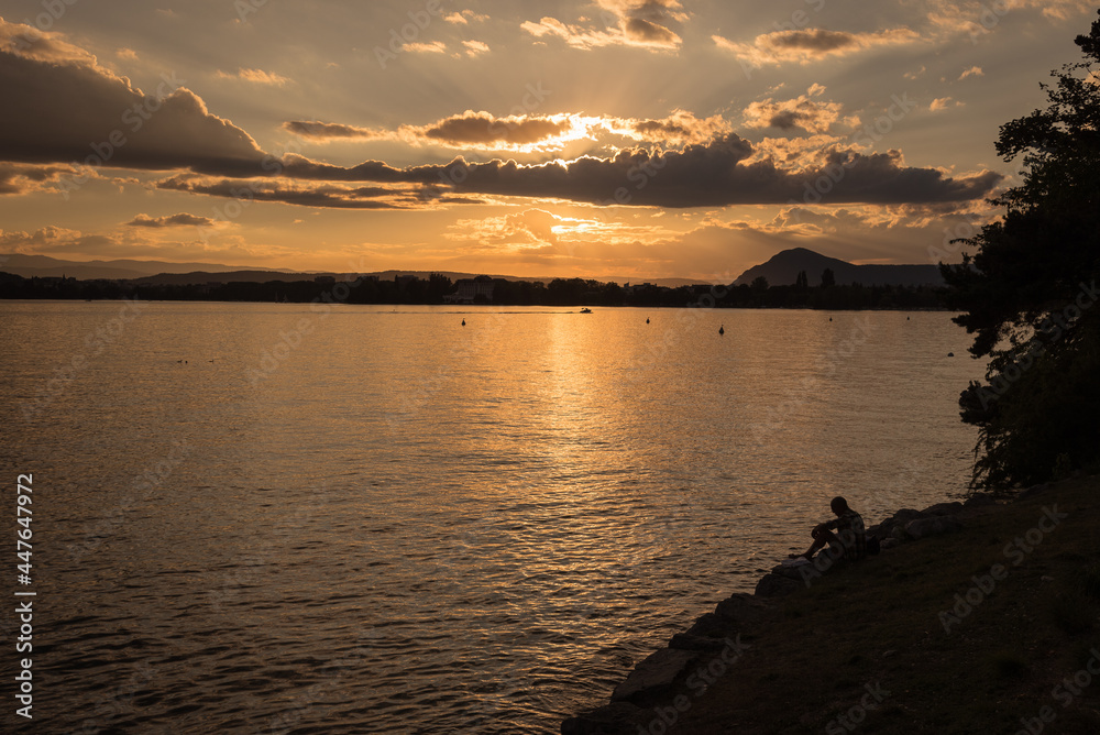 Scenic view of beautiful sunset with the sunlight reflected above the water of Annecy lake in summer with cloudy sky, France Scenic view of beautiful sunset with the sunlight reflected above the water of Annecy lake in summer with cloudy sky, France