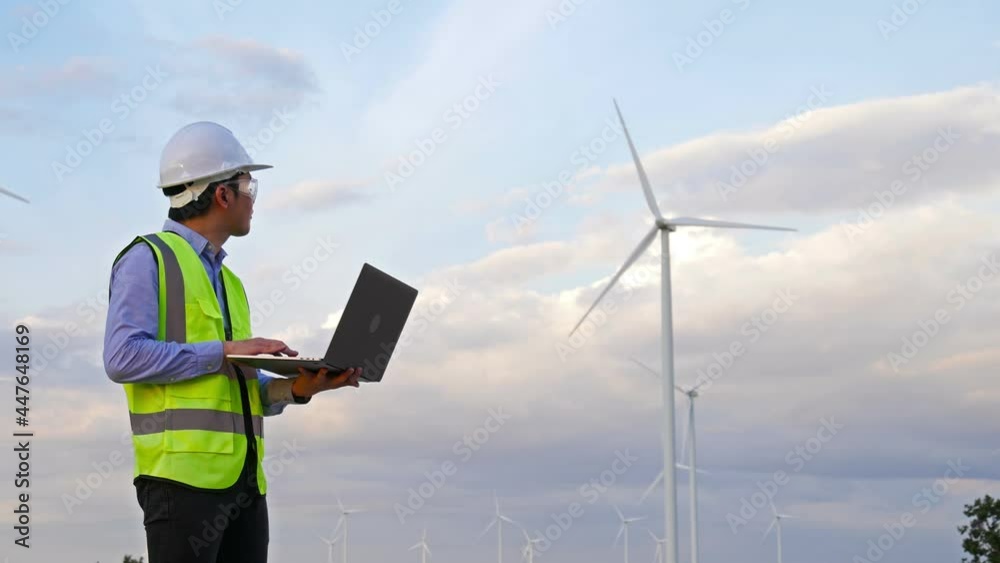 Young male engineer working with laptop computer against wind turbine farm. Young male engineer working with laptop computer against wind turbine farm.