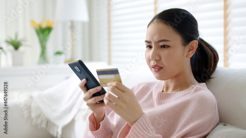 Valokuva Upset young asia teen girl sit at home sofa couch feel shock broke doubt annoy or lost money in e-commerce app error buy issue, wrong hoax digital wallet hacked or bad theft steal crime fraud banking