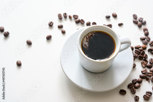 Hot coffee, black and strong in a white cup on a bright table with some beans, copy space, selected focus