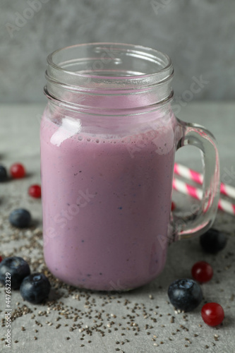 Glass jar of smoothie, ingredients and straws on gray textured table