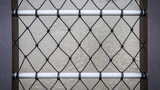 Fence decorated with black nylon net and silver rails. It is on a bridge over river.