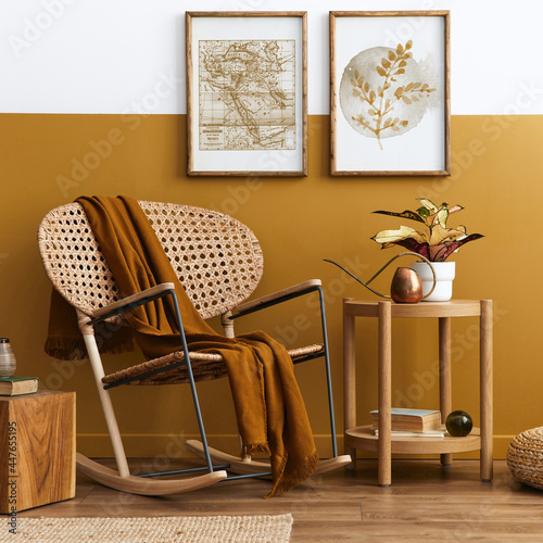 Stylish composition of living room interior with design rattan armchair, two mock up poster frames, plants, cube, palid and personal accessories in honey yellow home decor. Template. photo