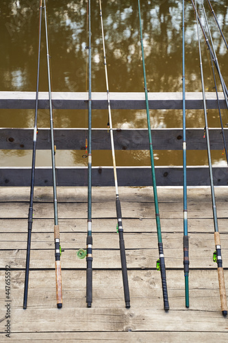 Many fishing rods on the wooden pier by the river or lake on a sunny day