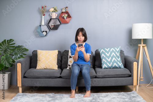 asian girl sit on couch in living room holding smart phone, chatting use social media network, watch received video from friend, with modern wireless technology.
